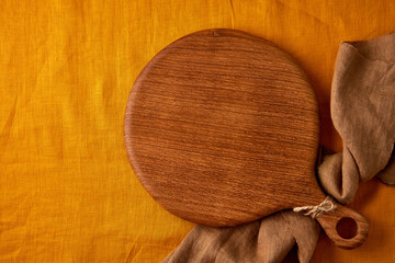 Food background mockup with round wooden cutting board on yellow, mustard linen textile tablecloth...