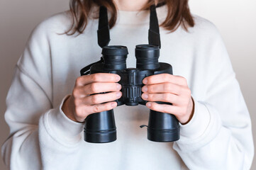 Woman's hands holding binoculars hanging on the neck. 