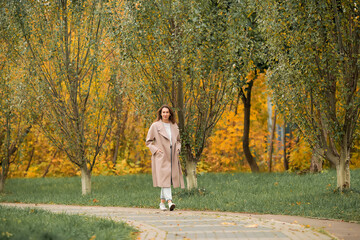 Fototapeta premium A Caucasian girl in a pink coat and blue jeans with holes dances in an autumn park