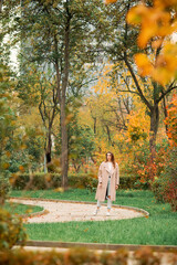 Fototapeta premium A Caucasian girl in a pink coat and blue jeans with holes dances in an autumn park