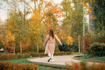 A Caucasian girl in a pink coat and blue jeans with holes dances in an autumn park