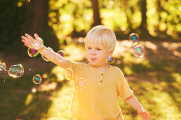 Outdoor portrait of adorable little boy playing with soap bubbles in summer park in sunlight, happy and healthy childhood