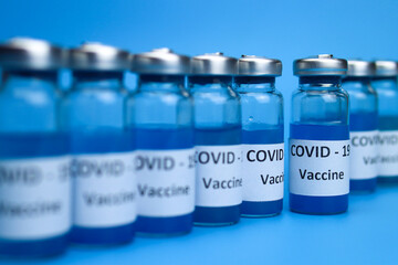 Ampoules with coronavirus vaccine in a row on a blue background. The concept of the fight against ncov COVID-19 pandemic
