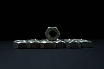 Nut bolts on a black background. threaded fastener. The nut bolts are stacked neatly in several rows, the rows tightly adjacent to each other. One nut is on top of the others