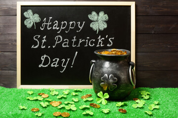 Banner, poster, invitation template. Happy St. Patricks Day chalk lettering on blackboard, cast iron pot full of leprechaun golden treasure, clover leaves and coins on green grass, dark wood bg