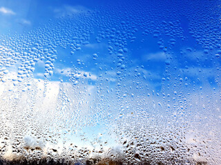 Water drops on the glass. Condensation on the window against the blue sky outside. Beautiful abstraction, romantic background.