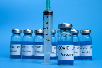 Ampoules with coronavirus vaccine and a syringe on a blue background. The concept of the fight against ncov COVID-19 pandemic