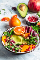 Buddha bowl of mixed vegetables and friit with avocado, persimmon, blood orange, nuts, spinach, arugula and pomegranate. Healthy balanced eating. Top view. vertical image
