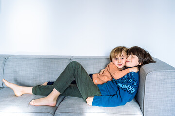 Obraz premium Two brothers lying on the couch at home, smiling and hugging. Good tender relationships between siblings. Embracing children.