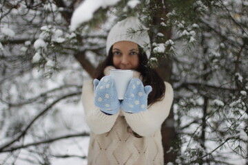 brown-haired girl drinking from a mug in the winter forest