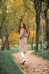 A European girl in a pink coat and blue jeans with holes walks in an autumn park
