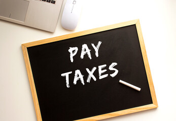 Text PAY TAXES written in chalk on a slate board. Office desk.