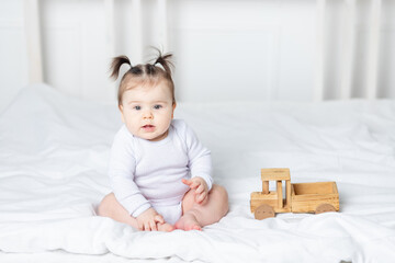 Fototapeta premium baby girl playing wooden toy typewriter on the bed at home, the concept of play and development of children