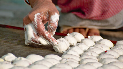 A bengali woman is making biuli dal bori on iron net surface. Bori is a form of dried lentil...