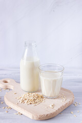 Vegetable oat milk in a glass bottle and in a glass cup on a wooden cutting board. Healthy drinks, vegetarianism. Side view. Vertical photo