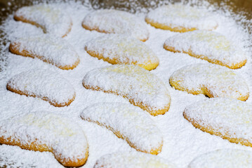Close-up of freshly baked cookies of the moon shape covered with powdered sugar. Freshly baked cookies on oiled baking paper. Selective focus, shallow depth of field.