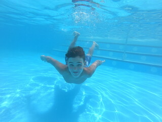 Boy swimming under blue water in pool