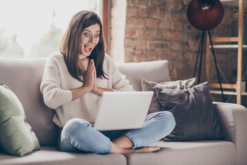 Photo of amazed happy woman clap hands read news laptop sit sofa wear jeans pullover inside home...