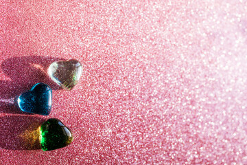 Three shining transparent glass hearts on the blurred pink background.