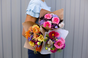 Woman in blue blouse holding beautiful bouquets of flowers. Hands with bouquets of seasonal flowers in craft paper. Bouquets as a gift. Orange and pink dahlia flowers