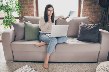 Photo of serious focused woman hold paperwork hand chin look laptop remote work inside home indoors house