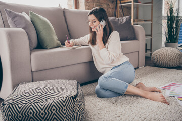 Fototapeta premium Full size profile side photo of brunette happy woman write note talk smartphone sit floor wear pullover jeans indoors inside house