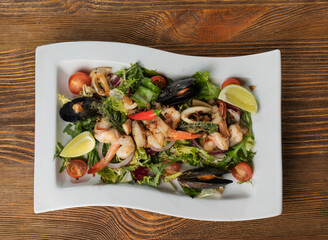 Close up of salad with seafood - shrimps, mussels, squid, vegetables and lemon in white plate on wooden table top view. High quality photo