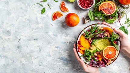 Fototapeta na wymiar Girl holding vegan, detox Buddha bowl with avocado, persimmon, blood orange, nuts, spinach, arugula and pomegranate, balanced food. space for text. top view
