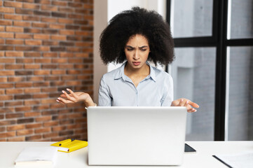 Confused and surprised young African-American businesswoman received unexpected news, sitting at...