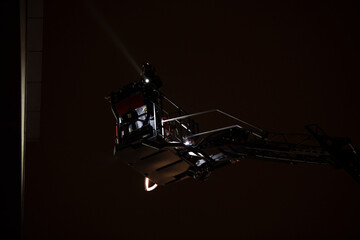 Fototapeta na wymiar Firefighters rise on a mechanical sliding ladder to the epicenter of the fire. Fighting fire from bucket atop a fire truck. A fireman's crane in action, silhouette against a dark night sky.