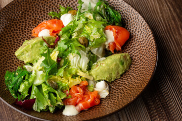 A salad with smoked salmon, mashed avocado and lettuce dressed with cream cheese. Close-up of the dish in a brown bowl isolated on wooden background. Horizontal orientation.