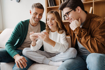 Happy gay family smiling and using mobile phone while sitting on couch