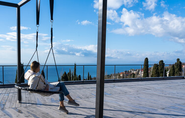Girl swinging on a swing admiring the sea on the horizon