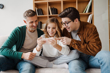 Happy gay family smiling and using mobile phone while sitting on couch