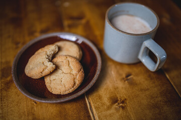 a delicious looking batch of snickerdoodle cookies and some warm milk in a rustic looking cup. the cookies are freshly baked and have   Cinnamon and sugar on them. the cow milk is fresh and warm. 