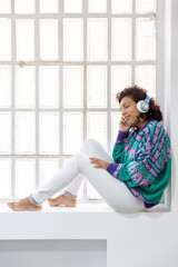 Portrait of brunette girl listening to music sitting on the window. Space for text.