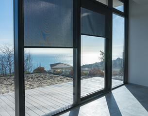 Sea view from the room of the new house through the panoramic windows with shutters. Minimalism and color trends in modern interiors