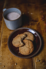 a delicious looking batch of snickerdoodle cookies and some warm milk in a rustic looking cup. the cookies are freshly baked and have   Cinnamon and sugar on them. the cow milk is fresh and warm. 