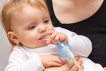 sick little girl makes inhalation with a nebulizer in her sister's hands.