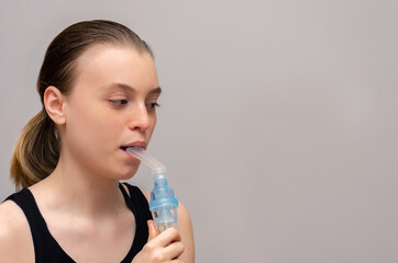 teenage girl with asthma and allergies makes inhalation with a medicine through a nebulizer in her hands on a gray background