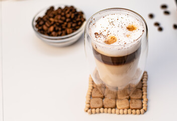 Glass thermal cup with coffee from a coffee machine on a white background. There are large coffee beans and a coffee machine next to the thermo mug.