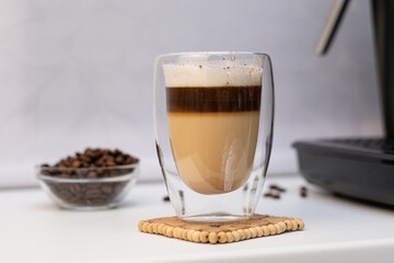 Glass thermal cup with coffee from a coffee machine on a white background. There are large coffee...