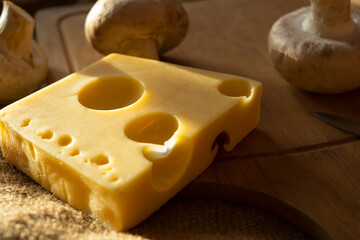 a piece of maasdam cheese, delicious cheese and mushrooms on a cutting board against a background of burlap