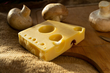 a piece of maasdam cheese, delicious cheese and mushrooms on a cutting board against a background of burlap