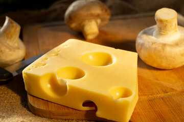 a piece of maasdam cheese, delicious cheese and mushrooms on a cutting board against a background of burlap