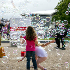 Group of joyful kids catching big soap bubbles while having party at green public park illuminated with sunbeams