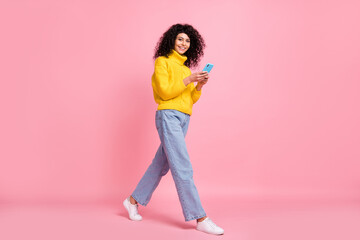 Full length photo of pretty cute wavy lady dressed yellow sweater walking chatting modern device isolated pink color background