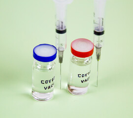 Glass vials with the text covid-19 vaccine medical syringes on a light green background. Medicine viral infection pandemic vaccines.