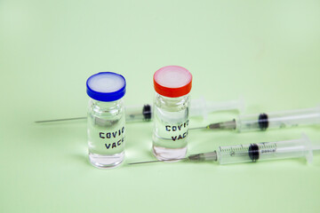 Glass vials with the text covid-19 vaccine medical syringes on a light green background. Medicine viral infection pandemic vaccines.