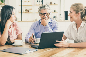 Happy female manager presenting project on laptop to young woman and mature man, discussing content with satisfied customers. Consulting or communication concept